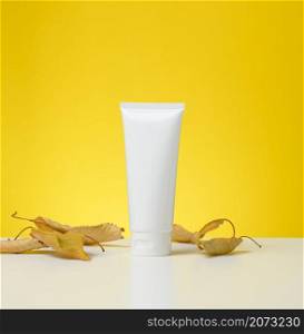 plastic tube with a lid on a white table, yellow background. Packaging for cosmetics, branding and product promotion