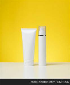 plastic white bottle with a dispenser and a tube with a lid on a white table, yellow background. Packaging for cosmetics, branding and product promotion