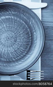 plate, knife and fork at napkin on wooden background