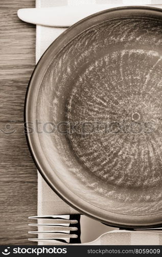 plate, knife and fork at napkin on wooden background