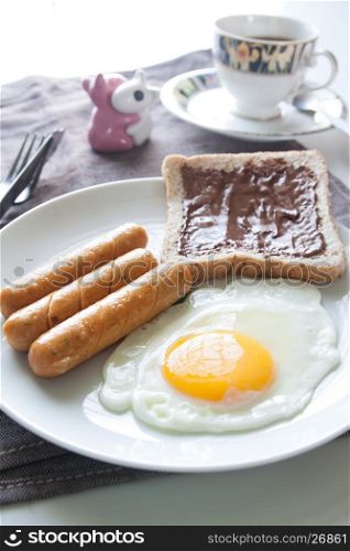 Plate of breakfast with egg, sausages, bread and chocolate cream on top