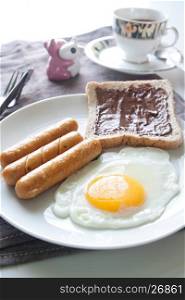 Plate of breakfast with egg, sausages, bread and chocolate cream on top