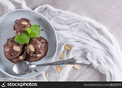 Plate of chocolate ice cream with almond slices and mint leaves.