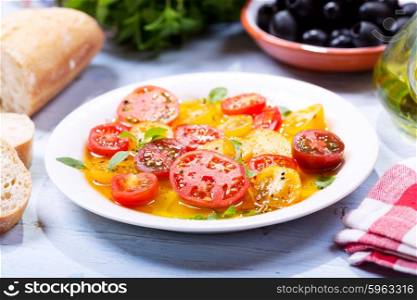 plate of colorful tomatoes with oil and basil on wooden table