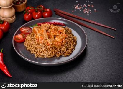 Plate of fried noodles and vegetables with hot chicken sauce on restaurant table, chinese cuisine. Thai noodle and chicken plate on a black concrete background with Chinese chopsticks and copy space
