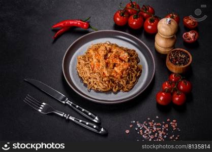 Plate of fried noodles and vegetables with hot chicken sauce on restaurant table, chinese cuisine. Thai noodle and chicken plate on a black concrete background with Chinese chopsticks and copy space