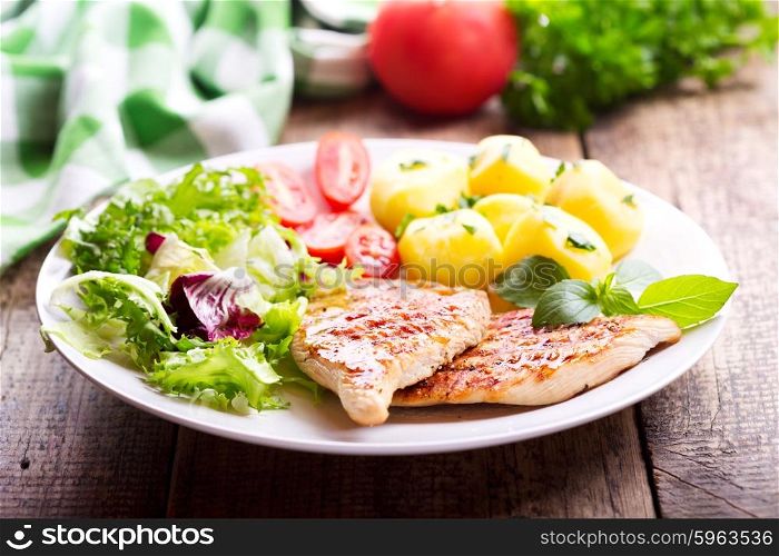 plate of grilled chicken breast with vegetables on wooden table