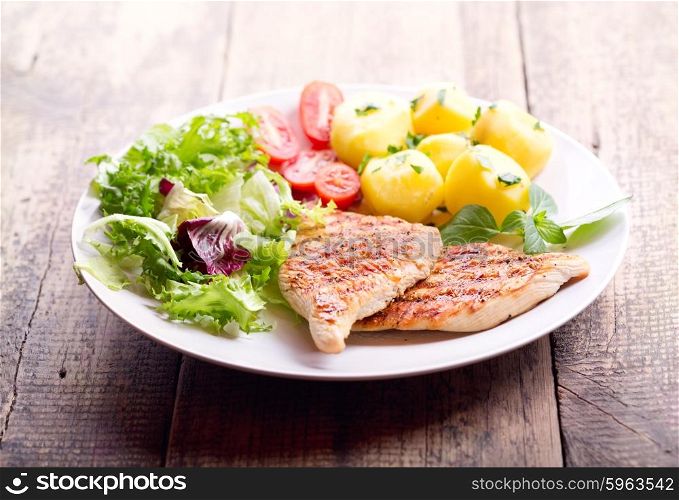 plate of grilled chicken breast with vegetables on wooden table