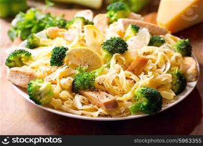 plate of pasta with chicken and broccoli on wooden table