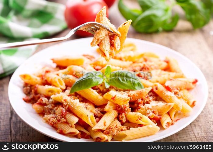 plate of penne pasta bolognese on wooden table