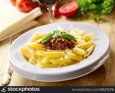 plate of penne pasta with bolognese sauce on wooden table