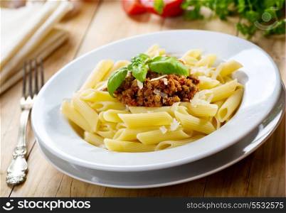 plate of penne pasta with bolognese sauce on wooden table