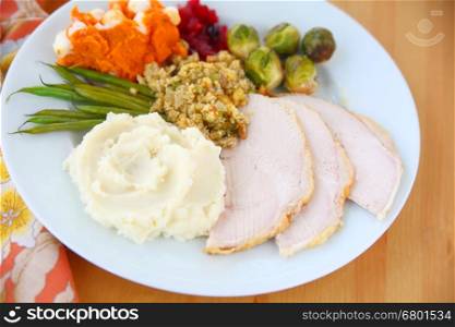 Plate of roast turkey slices, mashed potatoes, stuffing, brussels sprouts, mashed sweet potatoes and green beans with cranberry sauce