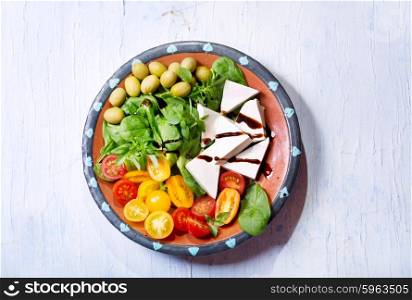 plate of salad with cheese, tomatoes, greens on wooden table, top view