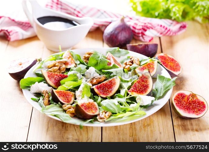 plate of salad with figs, arugula and feta cheese on wooden table