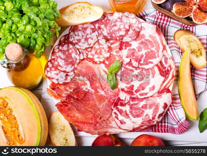 plate of various ham and salami with fresh fruits on wooden table