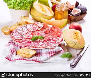 plate of various ham and salami with fresh fruits on wooden table