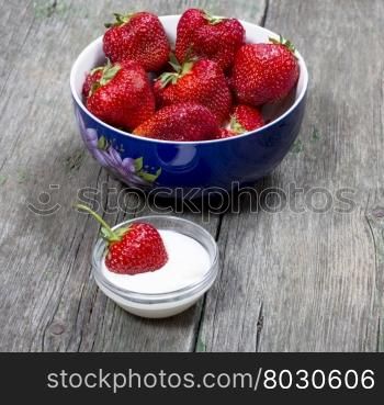 plate strawberry and one strawberry in a saucer with cream, on a wooden table, a subject of berry and desserts