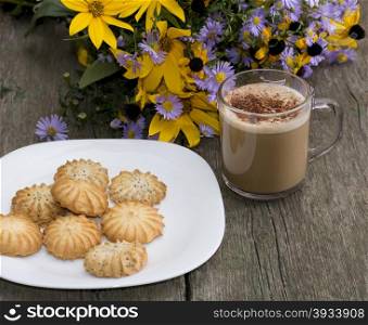 plate with cookies, a mug of a cappuccino and a bouquet of wild flowers on a wooden table, a still life on a subject fall and drinks