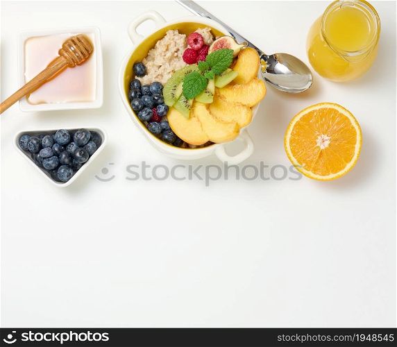 plate with oatmeal and fruit, half a ripe orange and freshly squeezed juice in a transparent glass decanter, honey in a bowl on a white table. Healthy breakfast