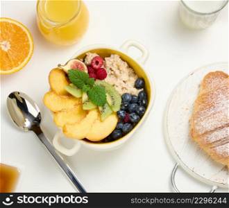 plate with oatmeal and fruit, half a ripe orange and freshly squeezed juice in a transparent glass decanter, honey in a bowl on a white table. Healthy breakfast, top view