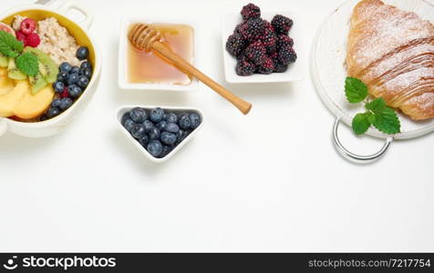 plate with oatmeal and fruit, half a ripe orange and freshly squeezed juice in a transparent glass decanter, honey in a bowl on a white table. Healthy breakfast