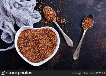 Plate with raw buckwheat on dark background