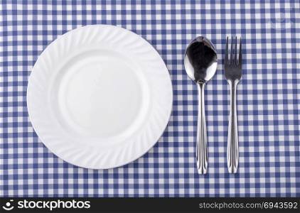 Plate with silverware on checquered blue background