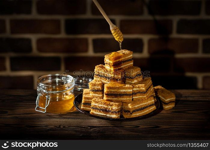 Plate with slices of honey cake and jar with honey on wooden table and brick wall background