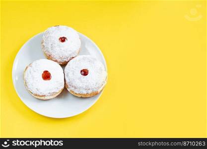 Plate with traditional Jewish dessert Sufganiyot on yellow background. Celebrating religious Judaism holiday. Donuts with jam and powdered sugar. Copy space.. Plate with traditional Jewish dessert Sufganiyot on yellow background. Celebrating religious Judaism holiday. Donuts with jam and powdered sugar.