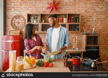 Playful black couple cooking romantic dinner on the kitchen. African family preparing vegetable salad at home. Healthy vegetarian lifestyle. Playful black couple cooking dinner on the kitchen