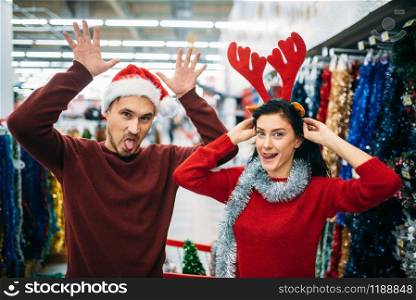 Playful couple choosing christmas decorations in supermarket, family tradition. December shopping of holiday goods. Playful couple choosing christmas decorations