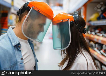 Playful couple choosing equipment in hardware store. Male and female customers look at the goods in diy shop