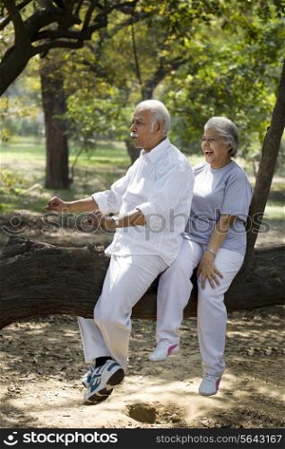 Playful couple having fun at park while sitting on tree trunk