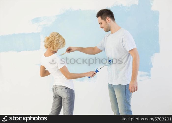 Playful couple painting each other in new house