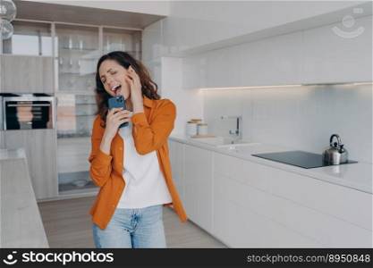 Playful girl is dancing alone at home. Excited european woman in airpods is singing and screaming with mobile telephone as with mic. App for music listening online. Happy housewife having fun.. Happy housewife having fun with mobile telephone. Playful girl is dancing and singing alone at home.
