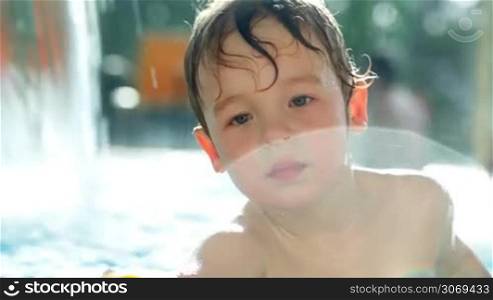 Playful little boy in the swimming pool splashing water then turning to his mom