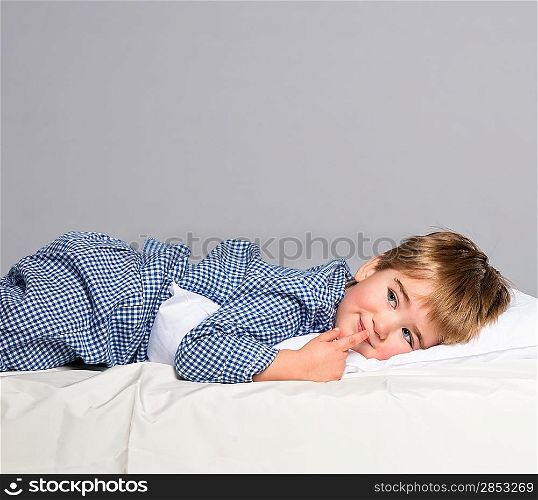Playful little boy wearing blue pyjamas in bed