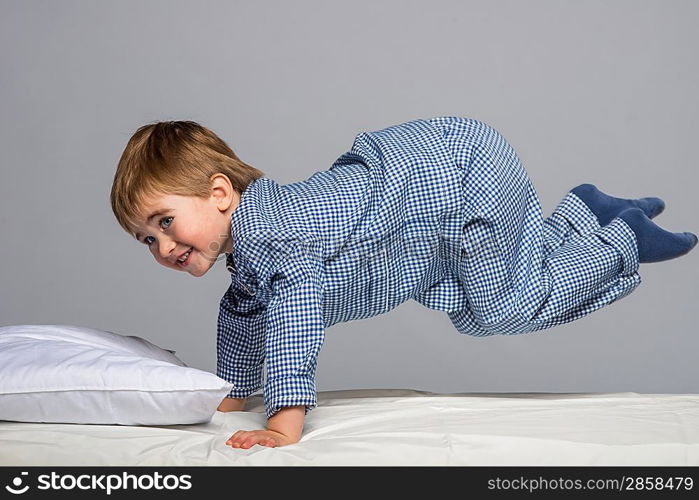 Playful little boy wearing blue pyjamas in bed