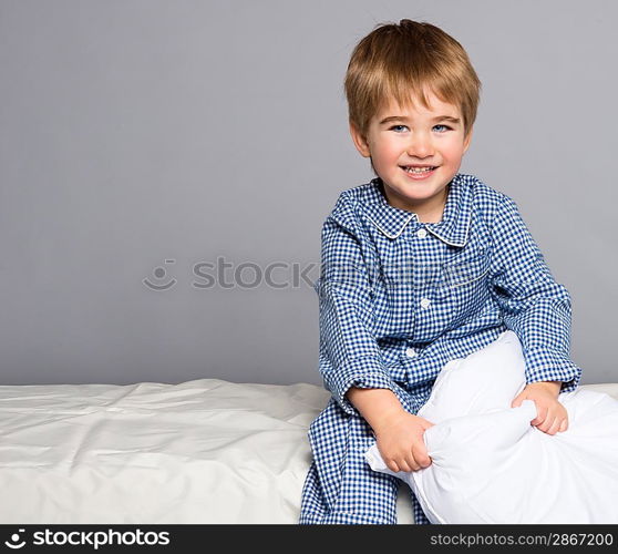 Playful little boy wearing blue pyjamas in bed