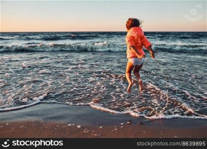 Playful little girl jumping over sea waves on a sand beach at sunset during summer vacation. Playful little girl jumping over sea waves on a sand beach at sunset