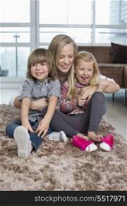 Playful mother with children sitting on rug in living room
