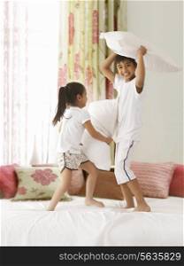 Playful siblings having pillow fight on bed
