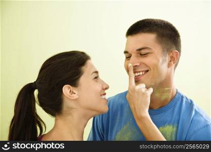 Playful smiling woman putting paint on man&acute;s nose.