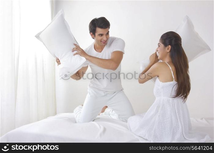 Playful young couple having pillow fight on bed