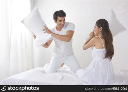 Playful young couple having pillow fight on bed