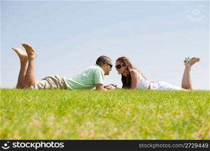 Playful young couple laying on a grass lawn and looking each otehr