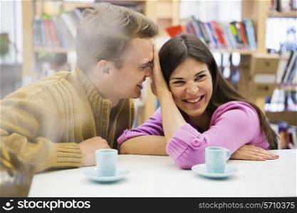 Playful young couple with coffee cups on desk in library