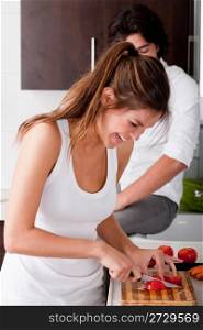 playful young girlfriend using chopping board for slicing tomatoes in kitchen