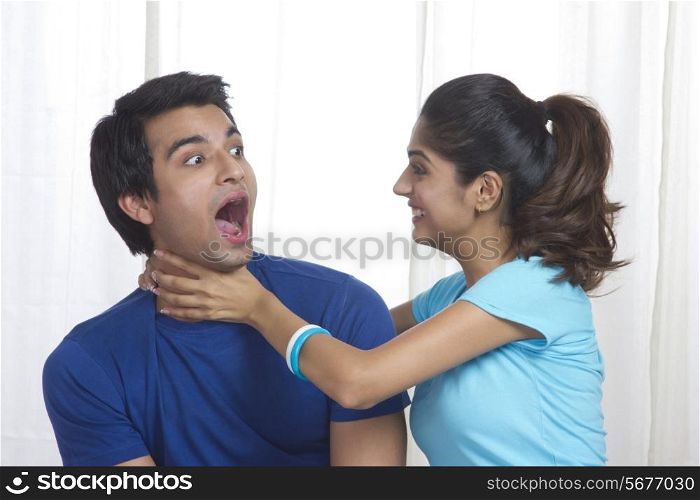 Playful young woman gripping man&rsquo;s neck at home